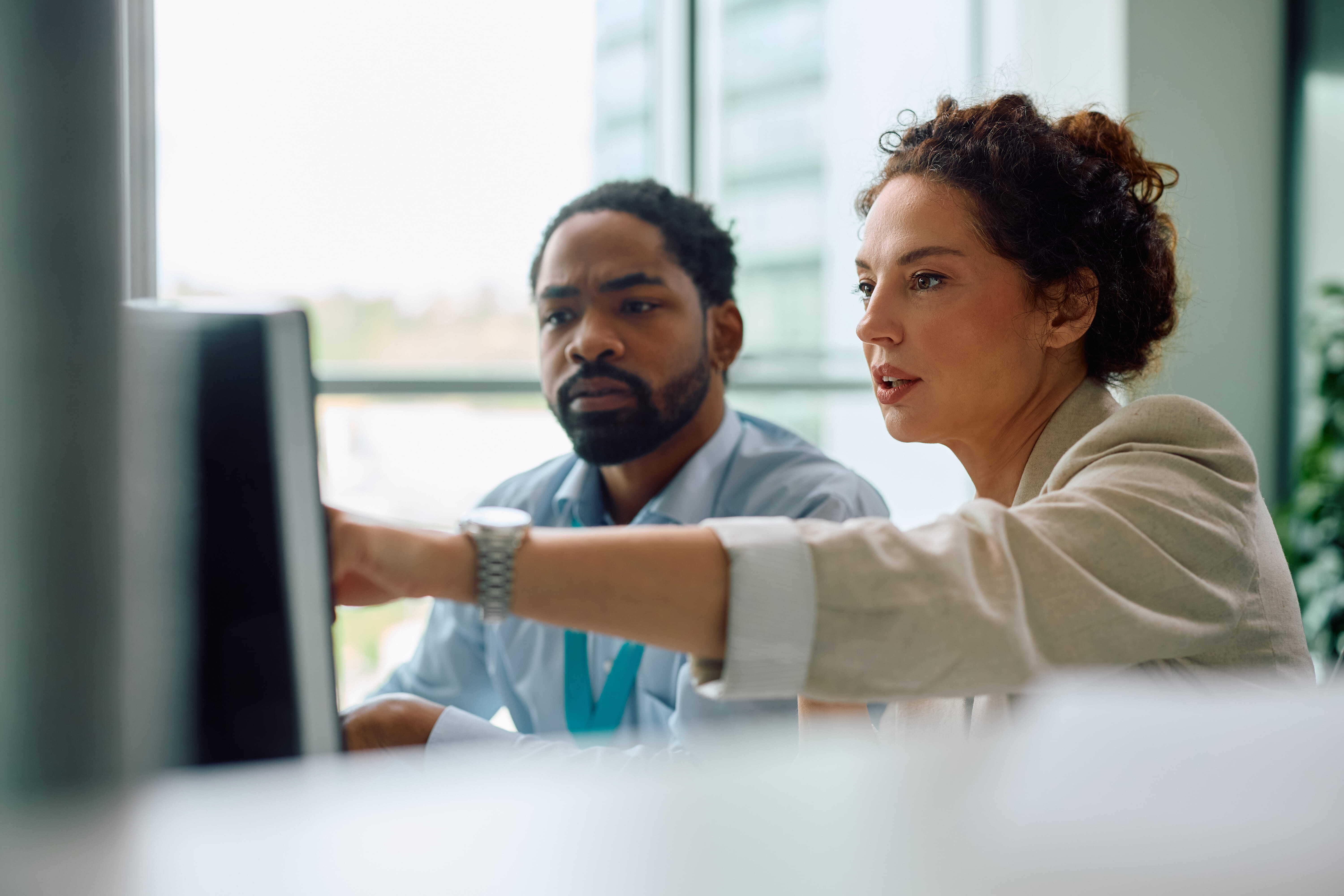Two colleagues looking at a computer screen while reviewing job ticketing software in an office.