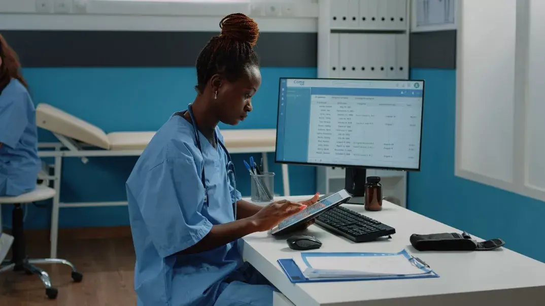 A nurse using a digital tablet in a healthcare facility to manage and track patient files.